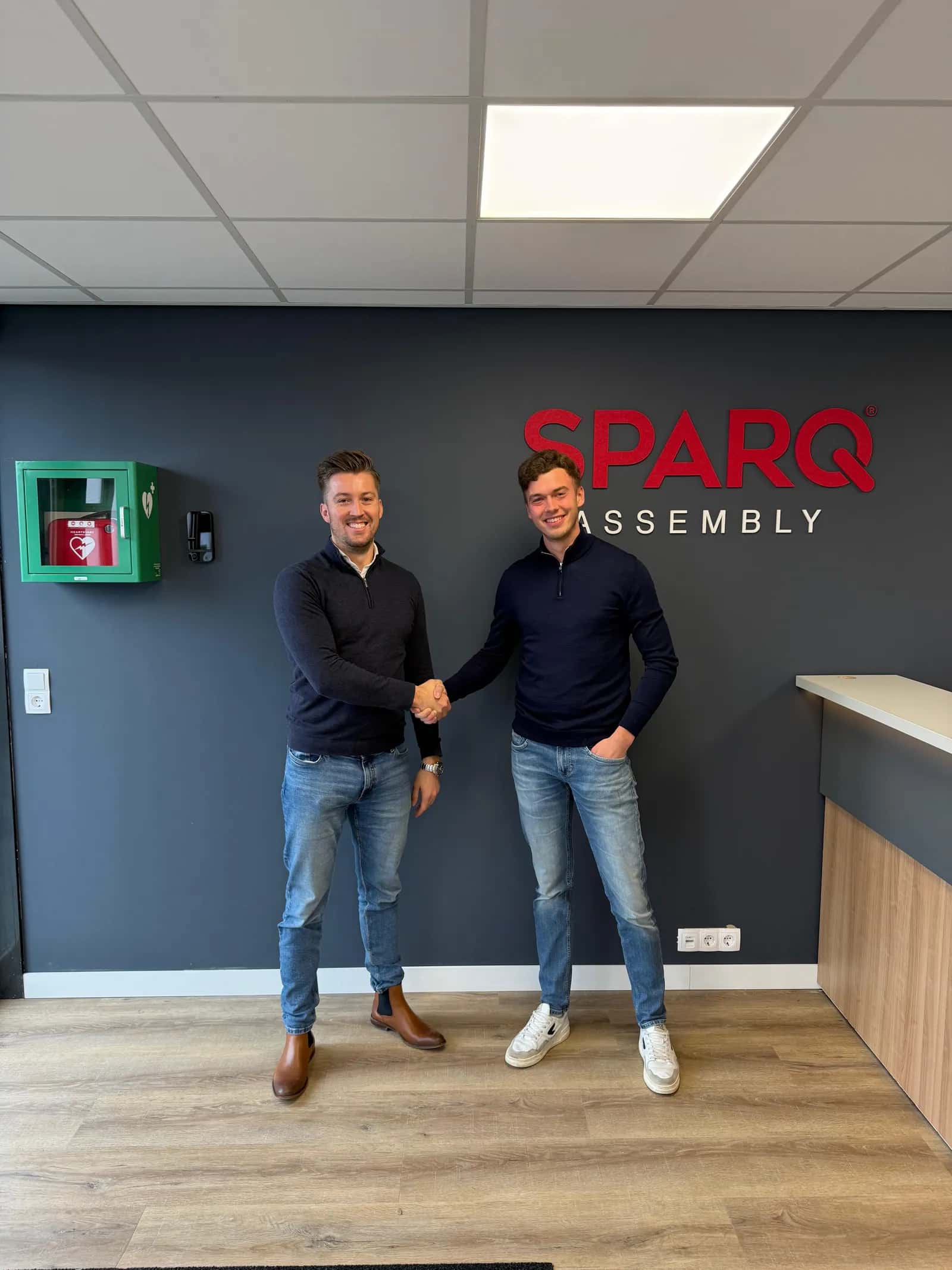 Twee mannen schudden elkaar de hand voor het logo van SPARQ Assembly